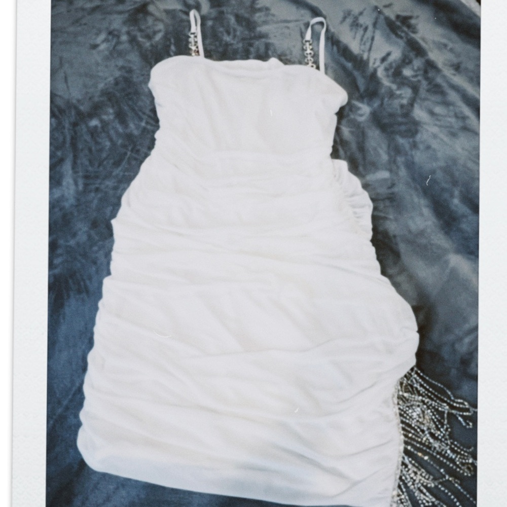 White mini bodycon dress with rhinestone straps and rhinestone fringe on leg